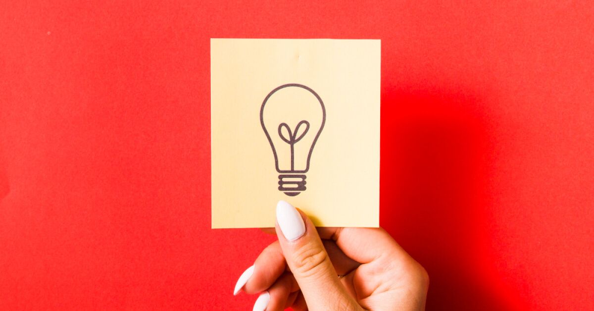 A woman holding a sticky note with a drawing of a light bulb