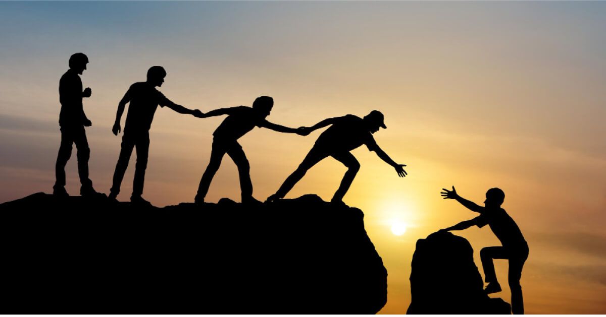 Group of people climbing mountain helping team member