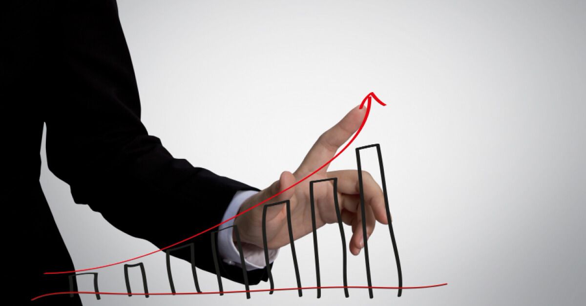 Person wearing suit placing their finger against a red upward arrow on a series of bar graphs