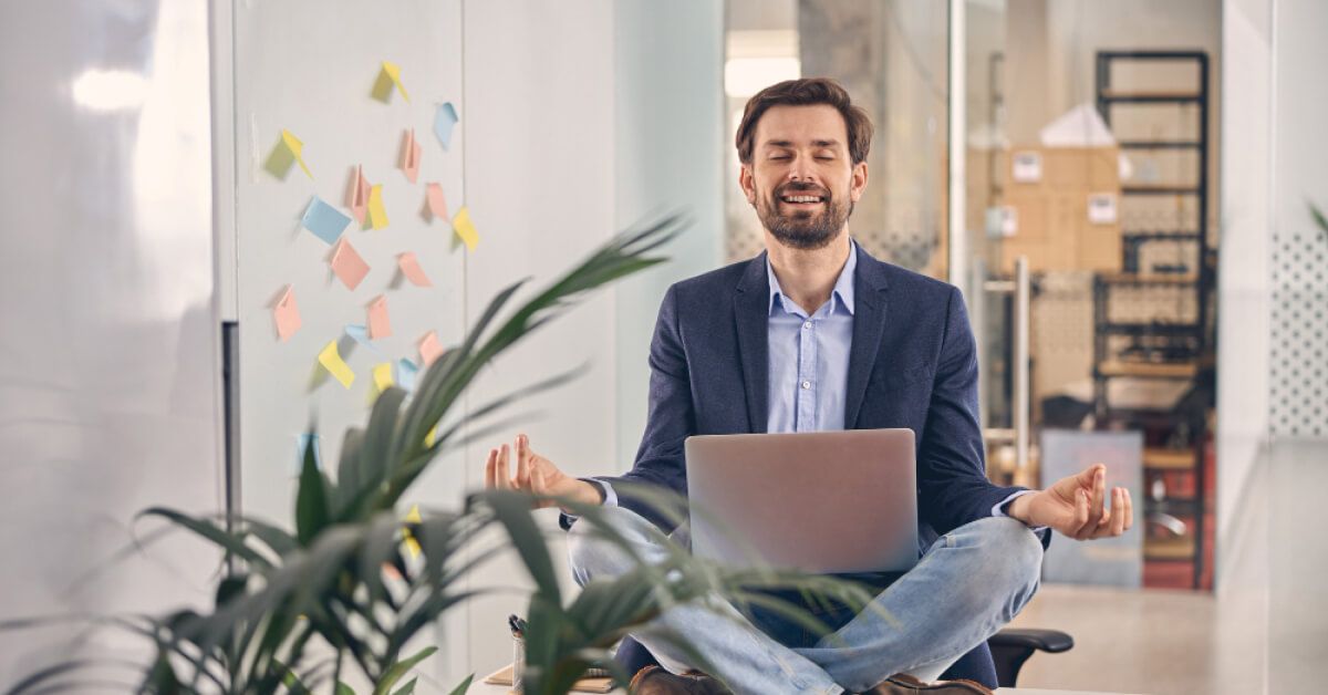 Person in an office with laptop, sitting in a meditative pose