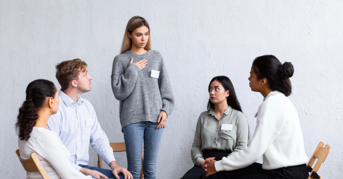 An individual speaking to a group of people sat together in a circle