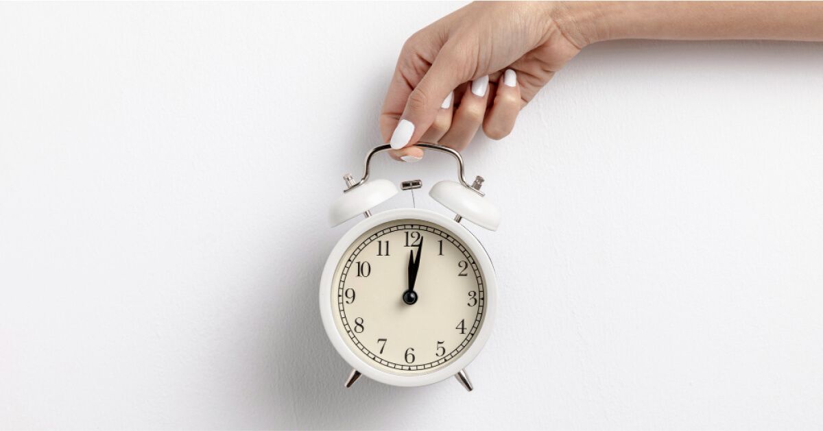 A hand holding an alarm clock over a white backdrop