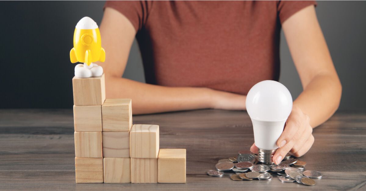 A lightbulb placed alongside some coins, wooden blocks as steps and a toy rocket