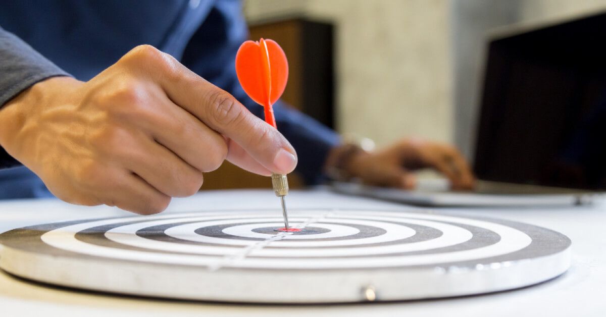 Person placing an orange dart on a target board that's laid flat