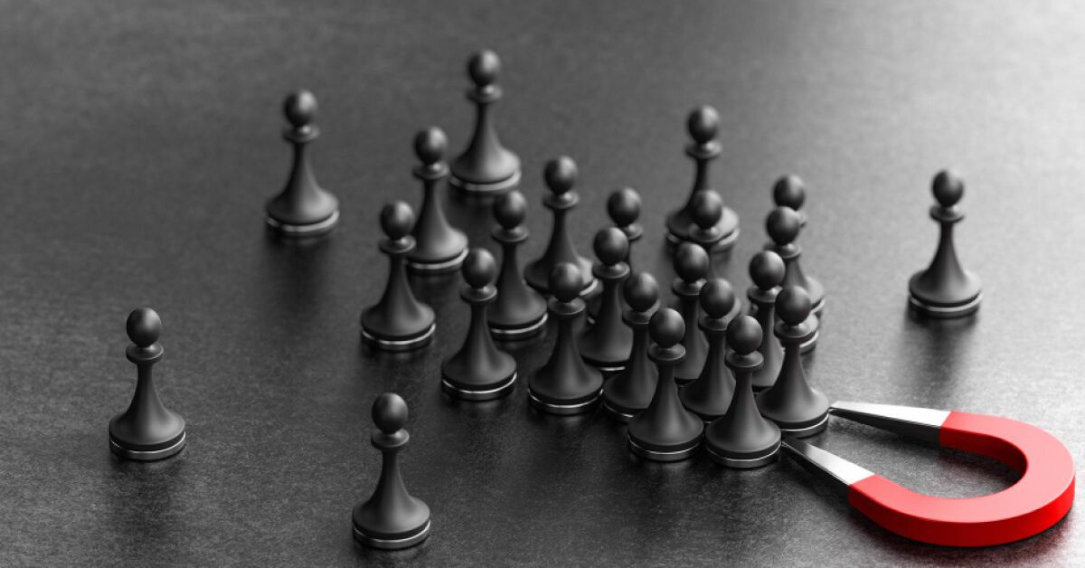 A horseshoe magnet attracting black chess pawns towards it