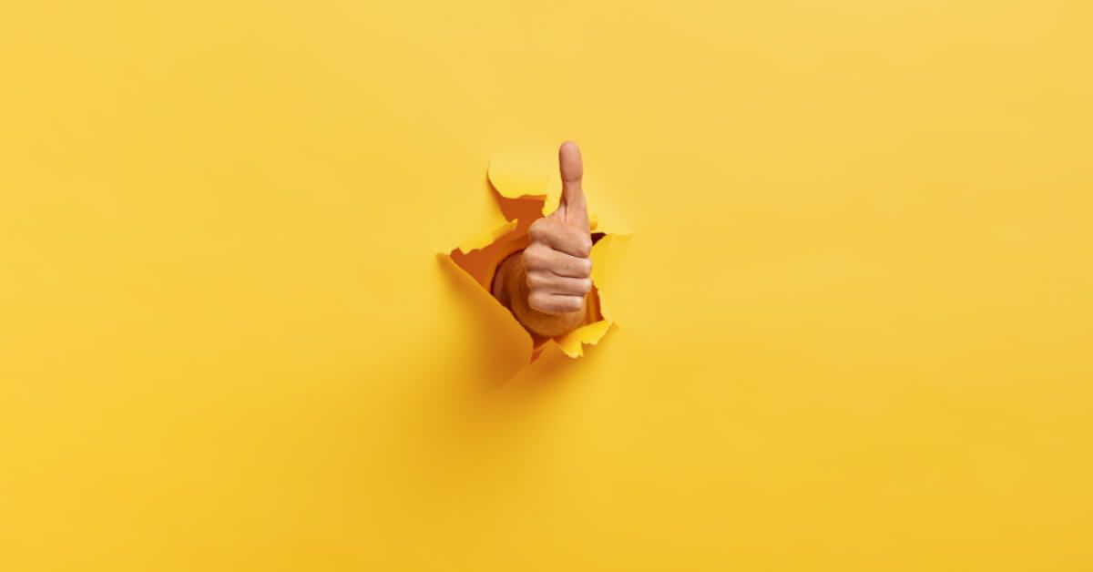 Man makes thumbs up gesture through a yellow paper wall