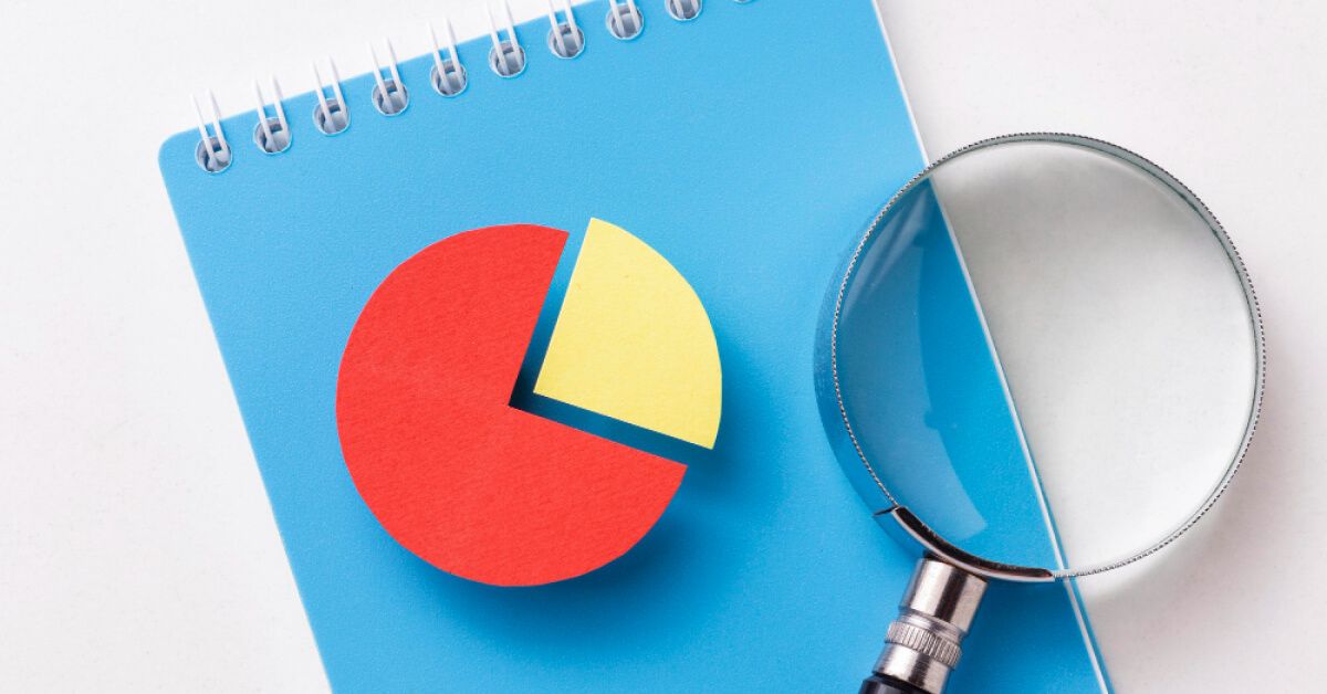 A magnifying glass placed over a blue notebook containing a pie chart