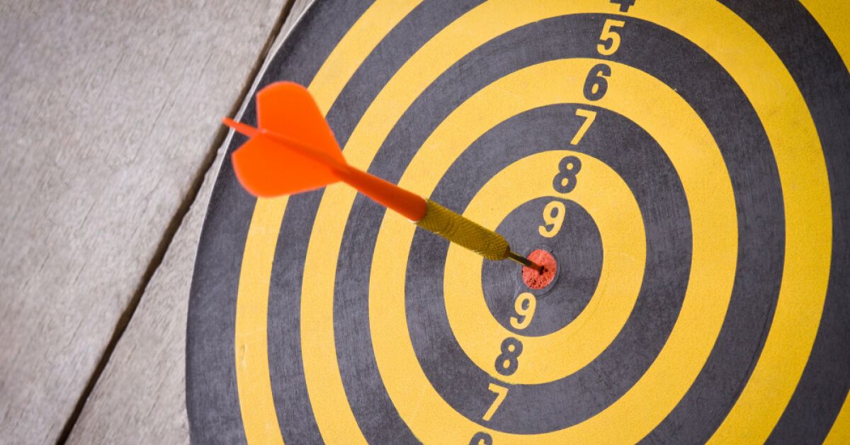 A dart hitting the bullseye on a yellow and black dart board