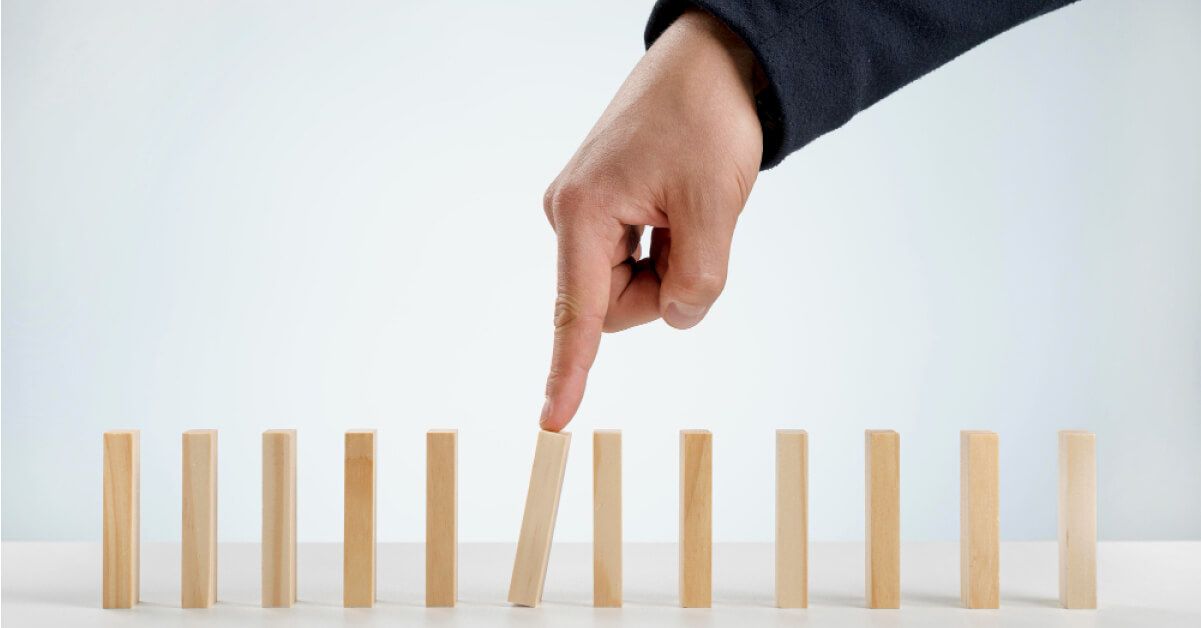 Person tipping over a wooden block that's placed along with other wooden blocks in a line