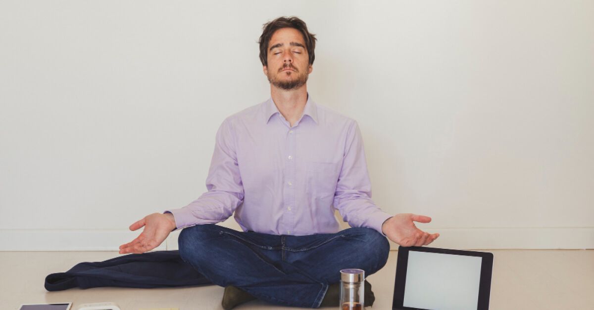 Man in a meditative pose with an open laptop next to him