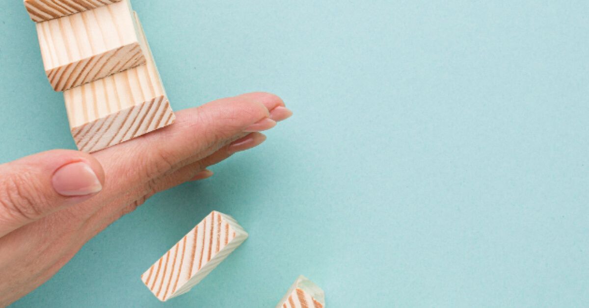 Person stopping a series of wooden blocks from falling over