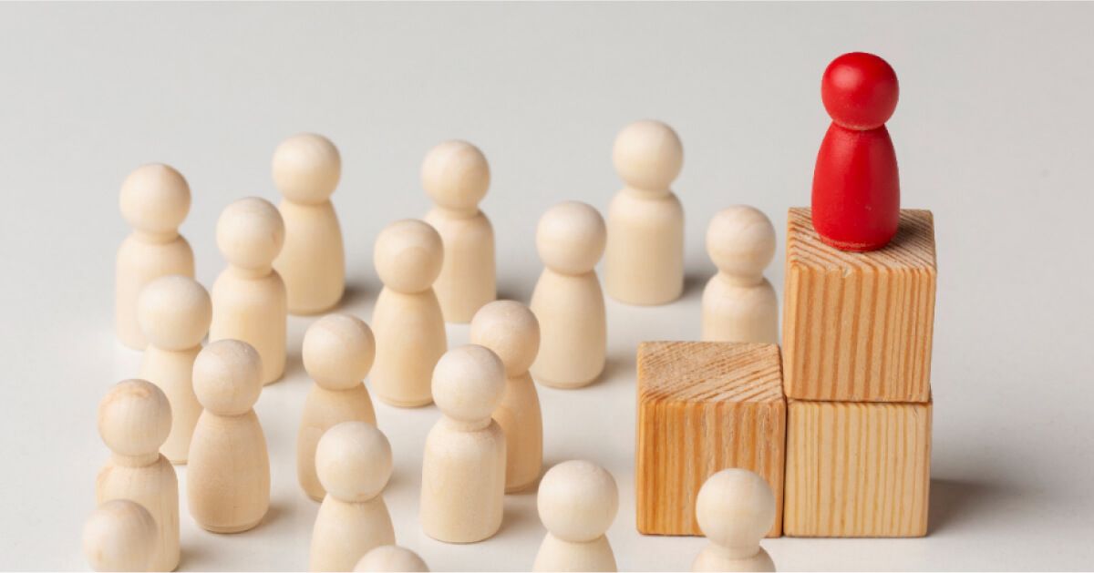 A red pawn on top of a set of wooden blocks, with white pawns around it