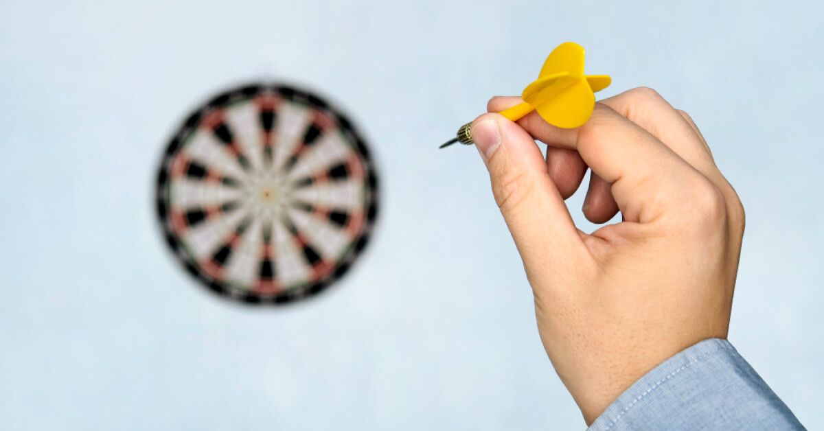 Person aiming a yellow dart at a dartboard target