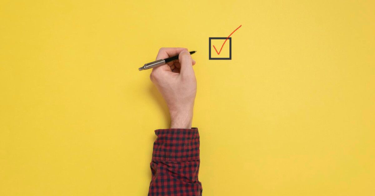 Person checking off a box against a yellow backdrop