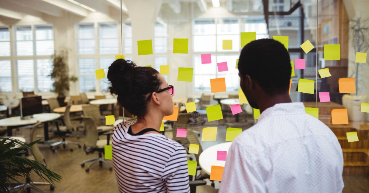 Two people in front of a series of post it notes on a glass wall