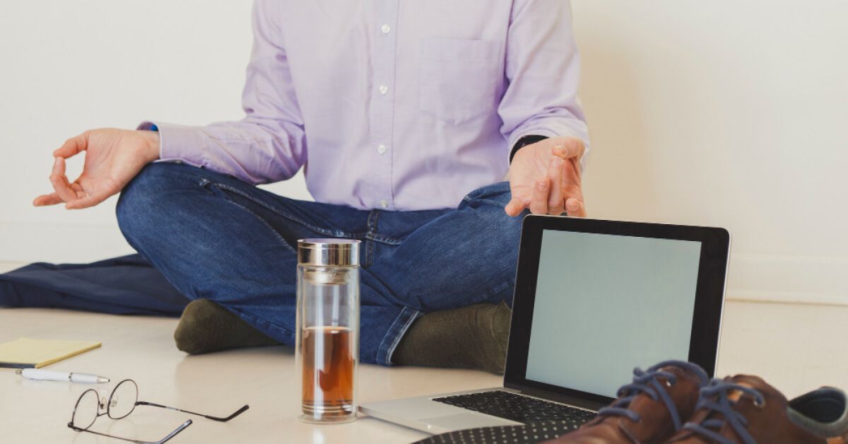 Person sitting in a meditative pose next to an open laptop