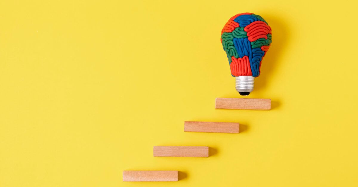 A light bulb made up by convoluted brain tubes, placed on a set of wooden blocks arranged in a stepwise manner