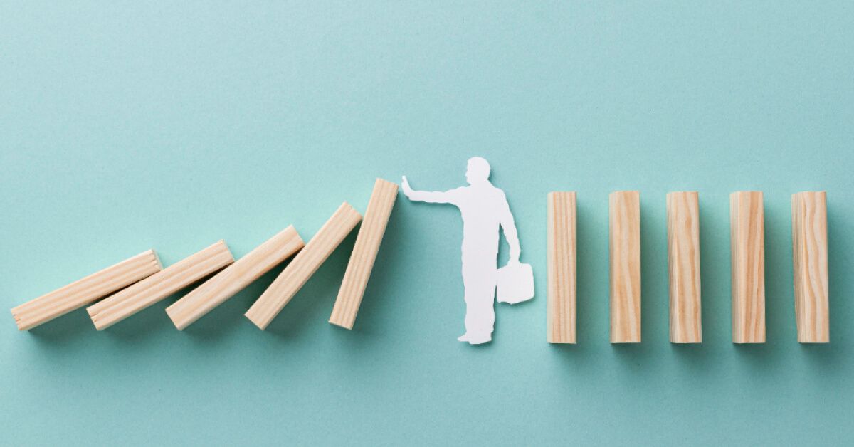 Paper cutout of a person stopping a series of wooden blocks from falling over