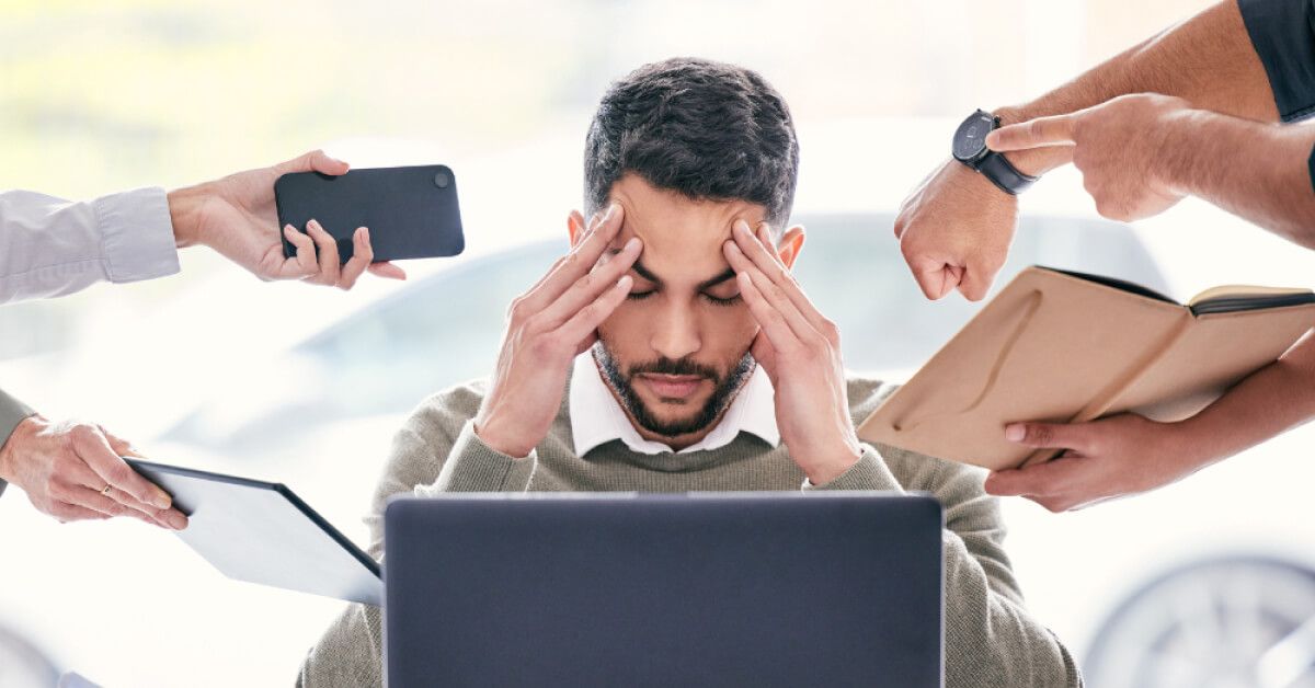 Stressed man in front of laptop, surrounded by other people