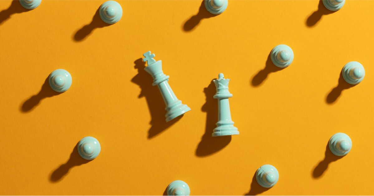 King and queen chess pieces laid flat against a yellow backdrop, surrounded by pawns