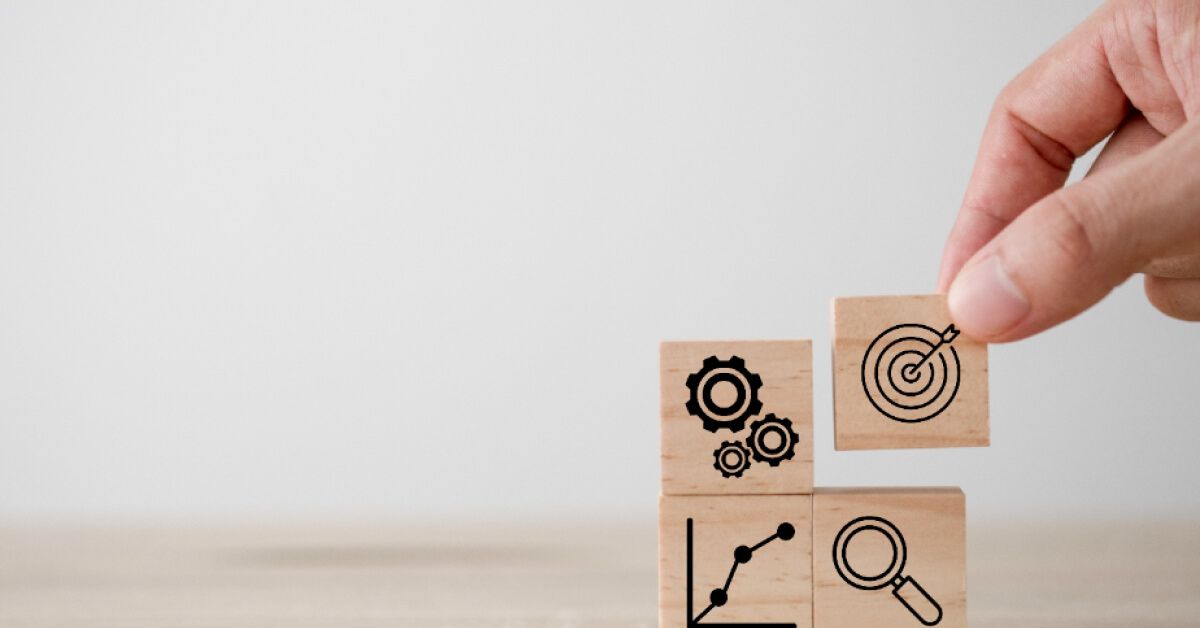 Person placing a wooden block with a target graphic into a grid of wooden blocks