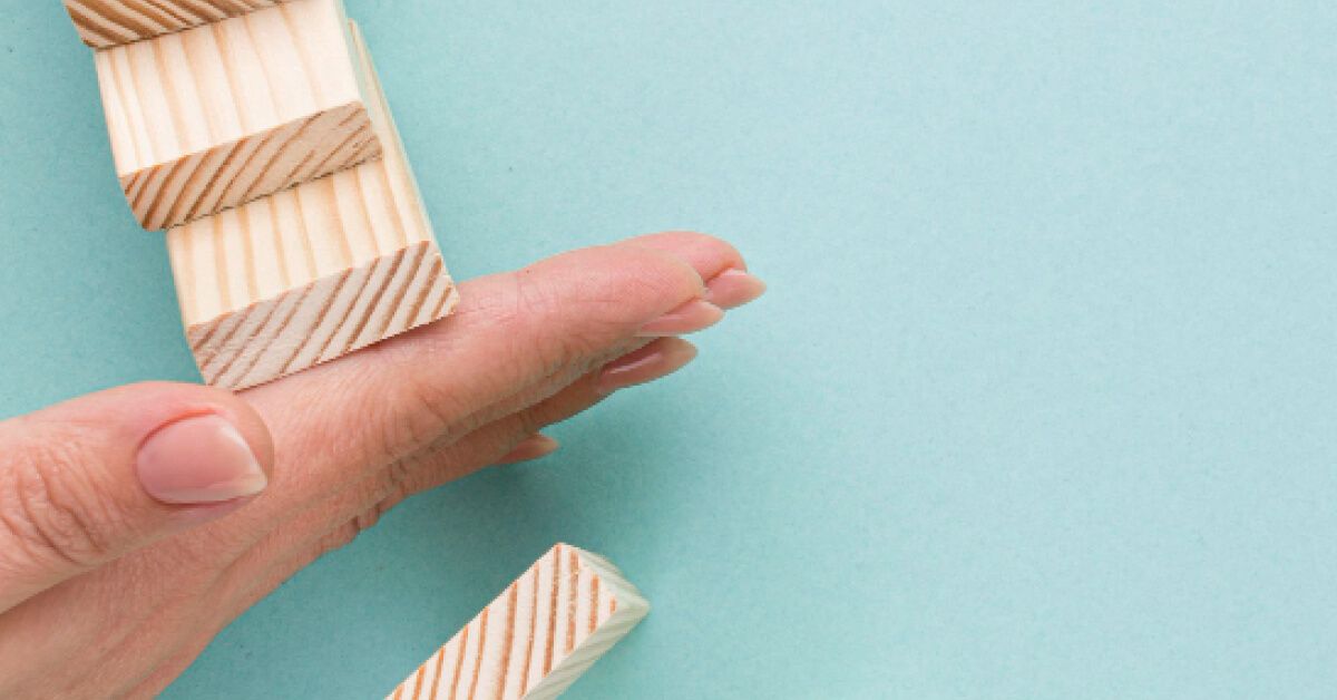 Person blocking a series of wooden blocks from falling over