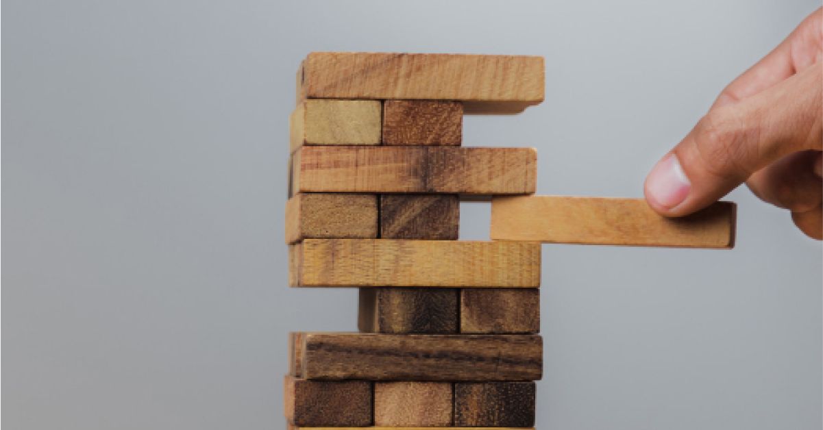 Person removing a wooden block from a tower of wooden blocks