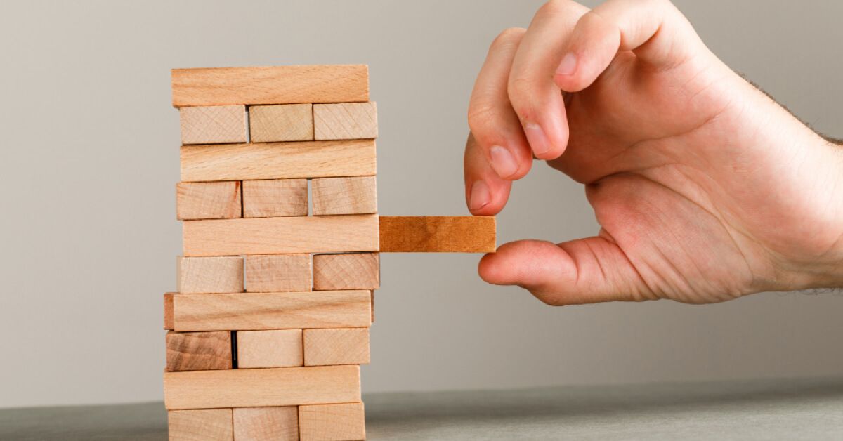 Person removing a wooden block from a tower of wooden blocks