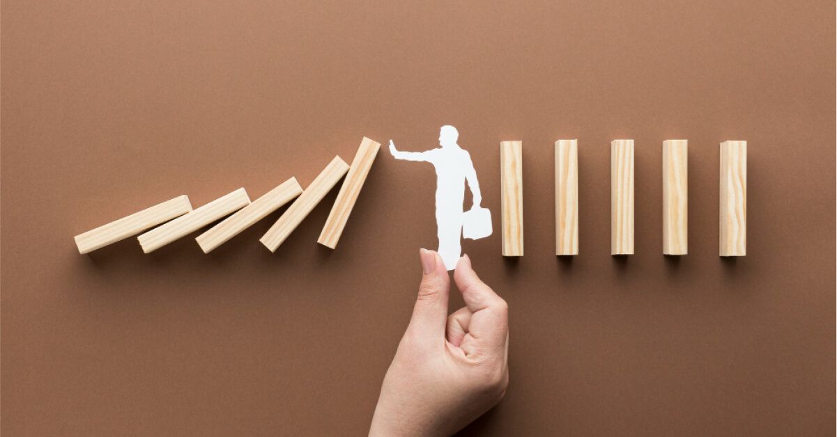 Paper cutout of a person stopping a series of wooden blocks from falling over