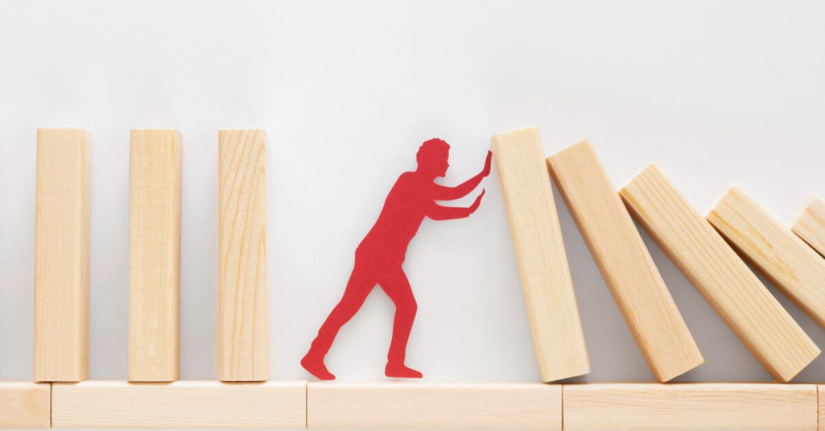 Red paper cutout of a person stopping a series of wooden blocks from falling