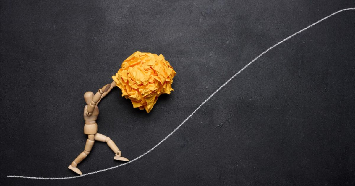 Wooden figurine pushing a crushed up yellow ball on a white upward line