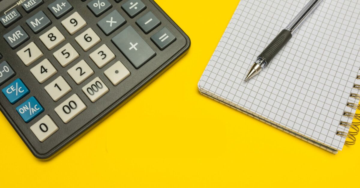 Calculator, pen and notepad against a yellow backdrop