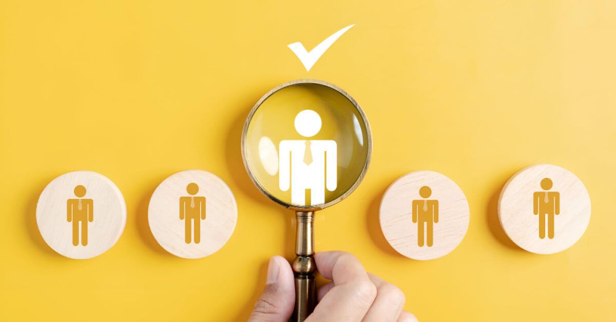 A magnifier glass overlooking an employee graphic amongst a line of other employees