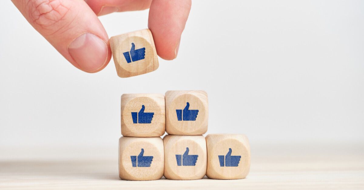 Person placing a wooden block with a thumbs up graphic on top of a set of wooden blocks