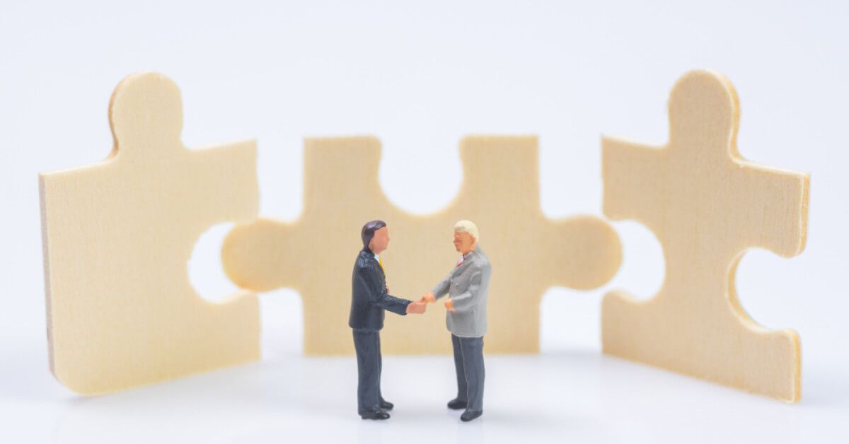 Two miniature businessmen shaking hands in front of three puzzle pieces