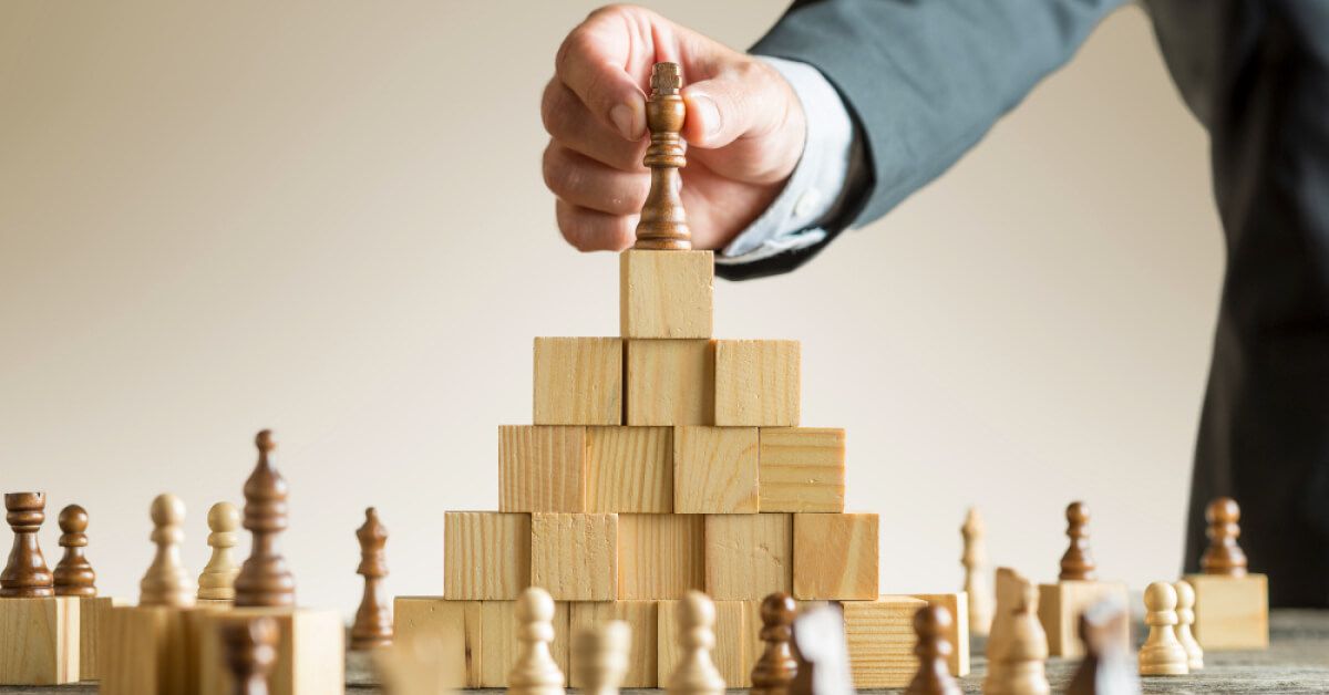 Business person placing a chess piece on top of a tower of wooden blocks