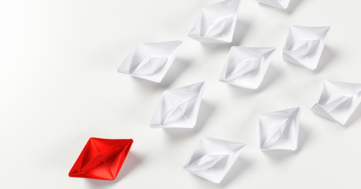 A red paper boat alongside a group of white boats