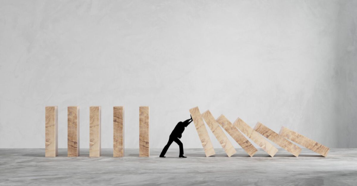 Silhouette of a person stopping a series of wooden blocks from falling over