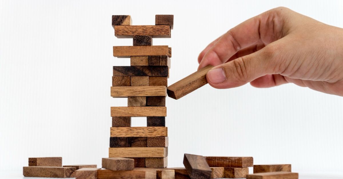 Person removing a wooden block from a tower of wooden blocks