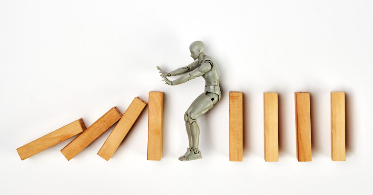 Miniature person blocking a series of wooden blocks from falling over