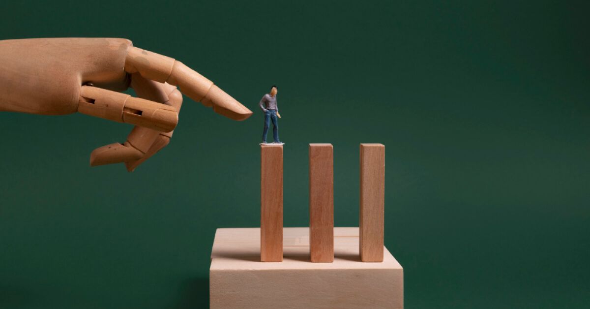 A wooden hand pointing at a miniature figurine thats placed over a wooden block