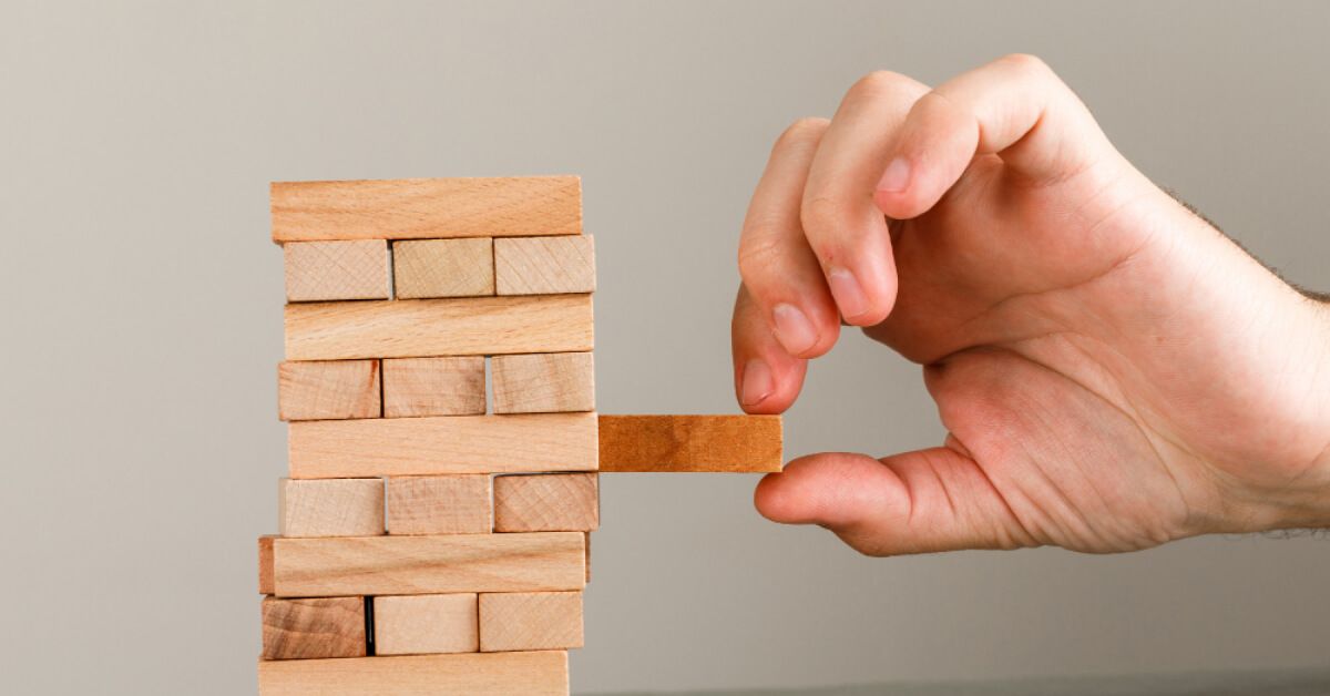 Person removing a wooden block from a tower of wooden blocks