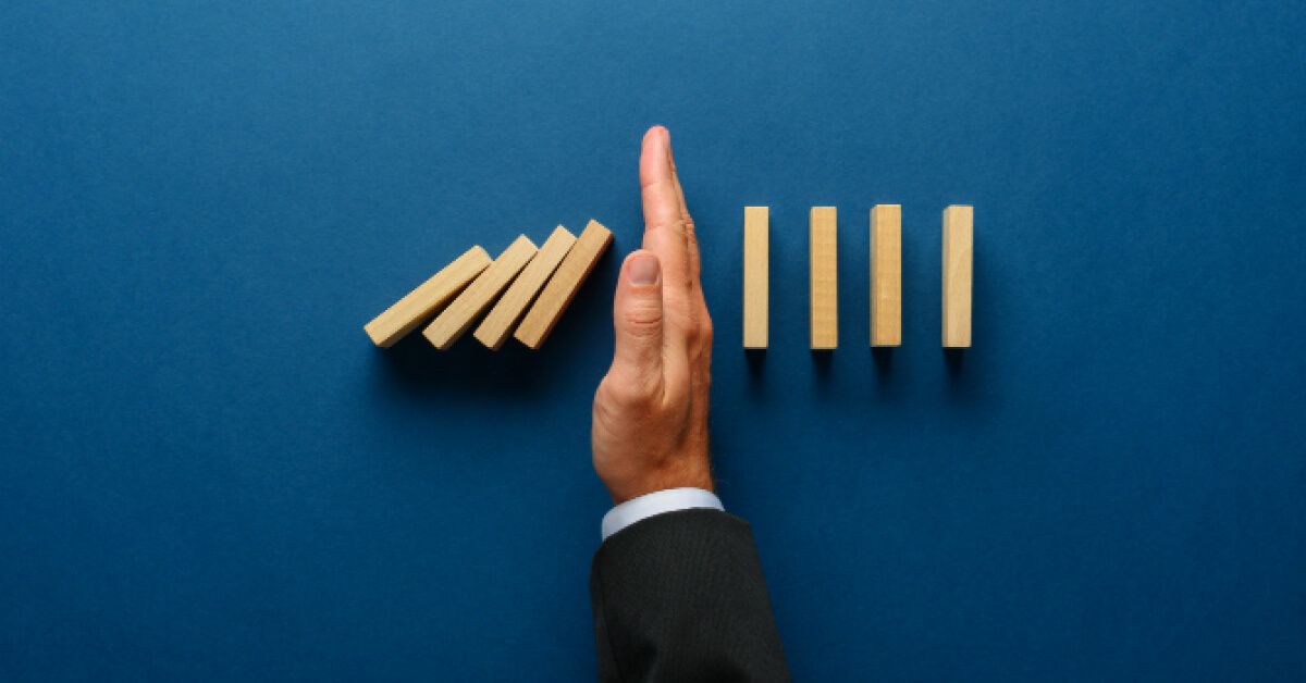 Person stopping a series of wooden blocks from falling over