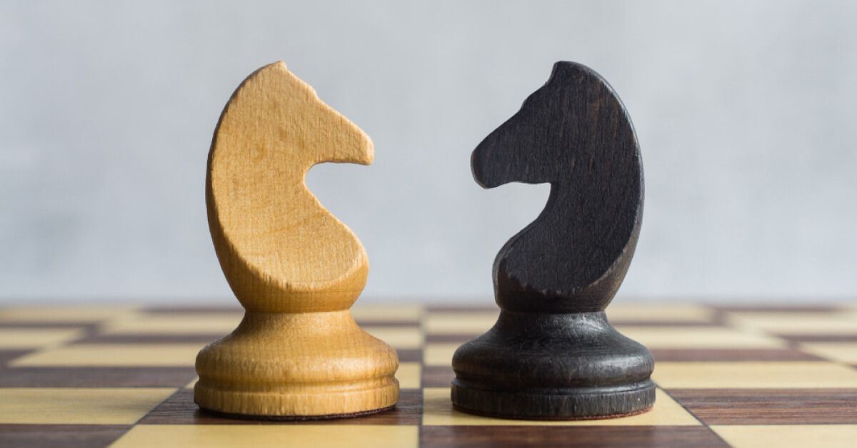 A black chess knight facing a white chess knight on a chessboard