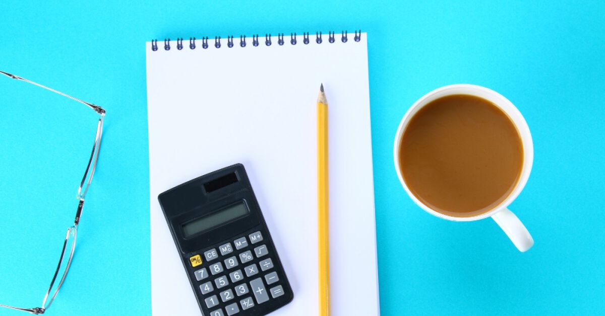 A calculator, pencil, notepad and spectacle next to a coffee mug