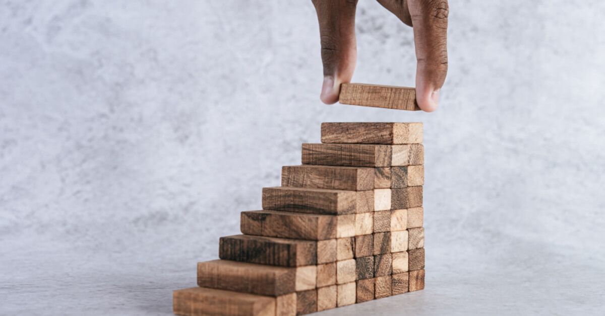 Person placing a wooden block on top of a set of wooden blocks arranged like steps