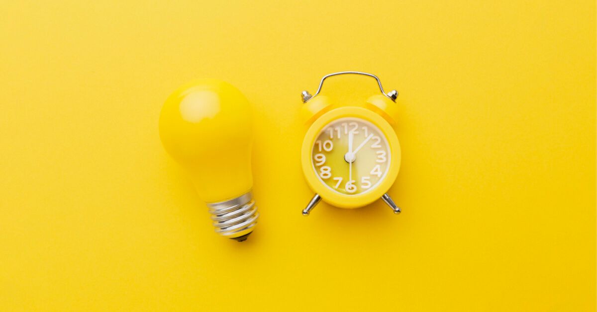 Yellow bulb and alarm clock against an yellow backdrop