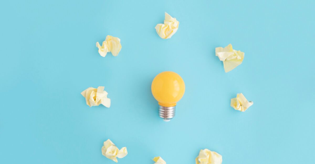 A group of crushed paper balls around a yellow lightbulb