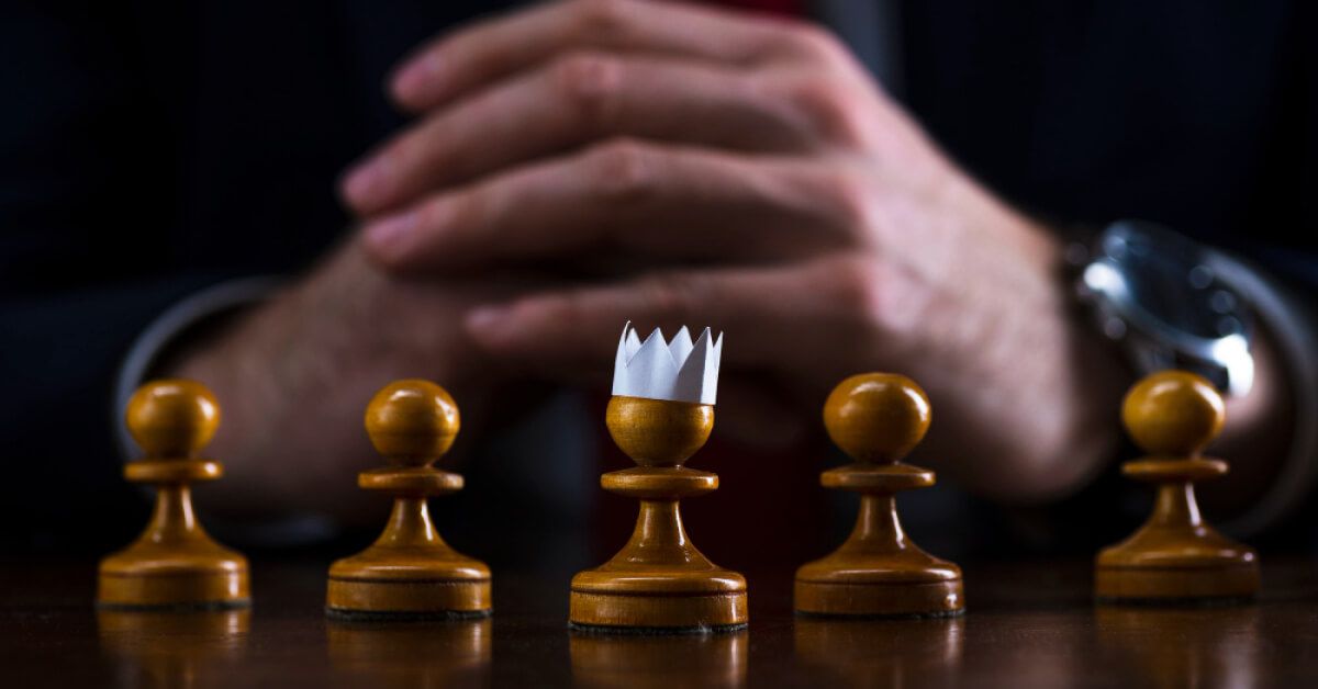 A set of chess pawns with a paper crown on one of them