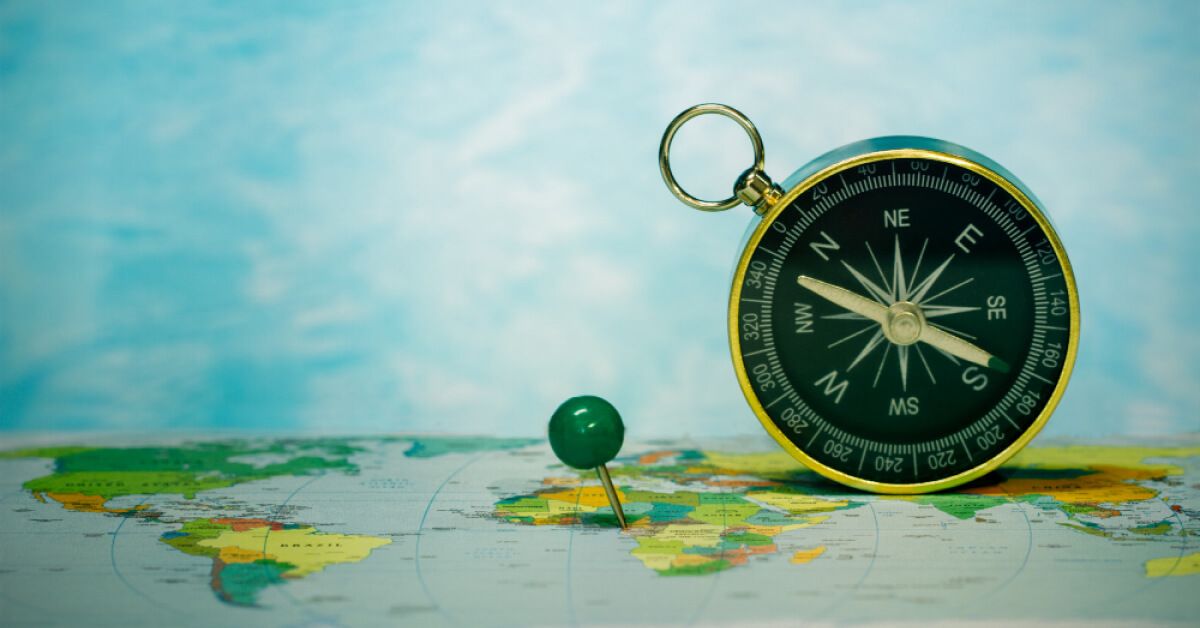 A green push-pin placed on a map with a metal compass next to it